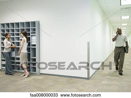 Office scene, two women talking by mailboxes while man using cell phone walks through hallway View Large Photo Image Stock Image - Office scene, two women talking by mailboxes while man using cell phone walks through hallway. Fotosearch