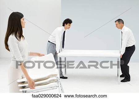 Professionals setting up office, men moving table, woman carrying chairs View Large Photo Image Picture - Professionals setting up office, men moving table, woman carrying chairs. Fotosearch