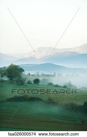 Picture - Rolling landscape with mist, mountains in the distance. Fotosearch