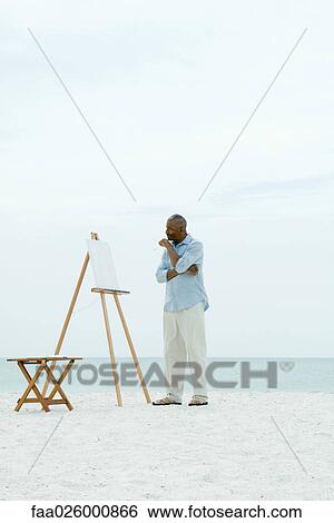 Senior man standing in front of blank canvas at the beach, holding paint brushes View Large Photo Image Stock Photograph - Senior man standing in front of blank canvas at the beach, holding paint brushes. Fotosearch