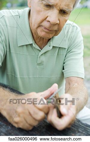 Stock Photograph - Senior man whittling piece of bark, close-up. Fotosearch