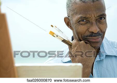 Senior man with hand under chin, holding paint brushes, smiling at camera, close-up View Large Photo Image Stock Image - Senior man with hand under chin, holding paint brushes, smiling at camera, close-up. Fotosearch