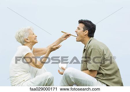 Senior woman feeding adult son with chopsticks, laughing, side view View Large Photo Image Stock Image - Senior woman feeding adult son with chopsticks, laughing, side view. Fotosearch