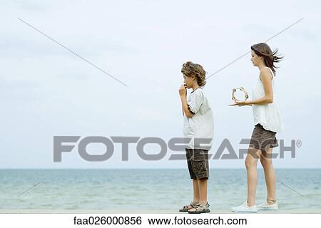 Siblings standing at the beach, boy playing harmonica, teen girl playing tambourine, looking at view View Large Photo Image Stock Photograph - Siblings standing at the beach, boy playing harmonica, teen girl playing tambourine, looking at view. Fotosearch