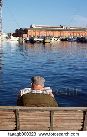 Spain, Barcelona, man sitting on bench reading newspaper by the water View Large Photo Image Stock Image - Spain, Barcelona, man sitting on bench reading newspaper by the water. Fotosearch
