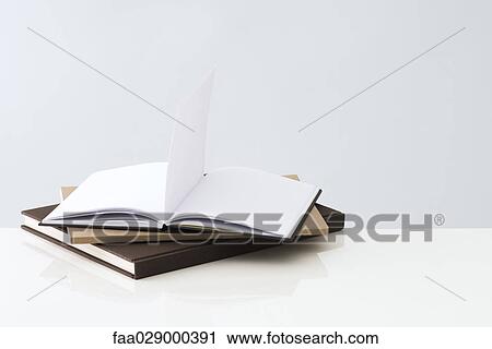 Stock Image - Stack of books, one open book with blank pages inside. Fotosearch