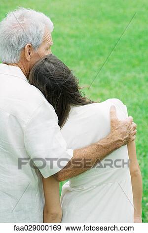 Stock Photo - Teen girl leaning head on grandfather's shoulder, rear view. Fotosearch