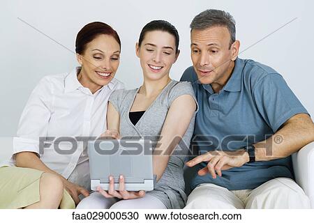 Stock Image - Teen girl watching portable DVD player with her parents, all smiling. Fotosearch