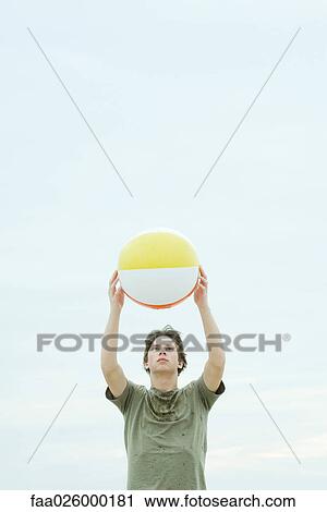 Teenage boy holding up beach ball, looking at camera View Large Photo Image Stock Image - Teenage boy holding up beach ball, looking at camera. Fotosearch