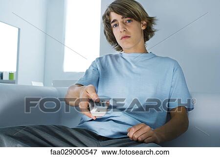 Teenage boy sitting on couch, holding remote control, looking at camera View Large Photo Image Stock Photo - Teenage boy sitting on couch, holding remote control, looking at camera. Fotosearch