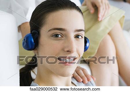 Teenage girl listening to headphones, smiling at camera, woman's hand on her shoulder View Large Photo Image Stock Image - Teenage girl listening to headphones, smiling at camera, woman's hand on her shoulder. Fotosearch
