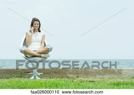 Teenage girl sitting in chair by the sea, using cell phone, smiling at camera View Large Photo Image Stock Image - Teenage girl sitting in chair by the sea, using cell phone, smiling at camera. Fotosearch