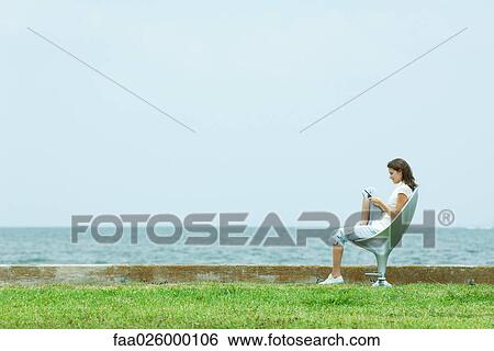 Teenage girl sitting in chair by the sea, looking down at cell phone, side view View Large Photo Image Stock Photograph - Teenage girl sitting in chair by the sea, looking down at cell phone, side view. Fotosearch