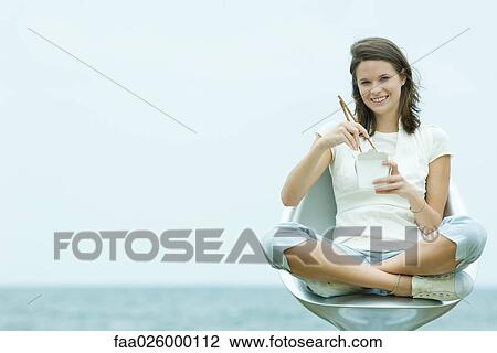 Teenage girl sitting in chair, holding chopsticks and take out food container, smiling at camera View Large Photo Image Stock Image - Teenage girl sitting in chair, holding chopsticks and take out food container, smiling at camera. Fotosearch