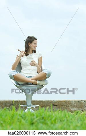 Teenage girl sitting in chair outdoors, holding chopsticks and take out food container, looking away View Large Photo Image Stock Image - Teenage girl sitting in chair outdoors, holding chopsticks and take out food container, looking away. Fotosearch