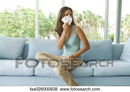 Stock Photo - Teenage girl sitting on couch, holding cards in front of face, looking away. Fotosearch