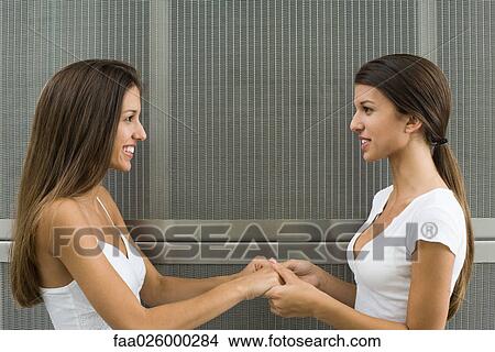 Teenage twin sister face to face, holding hands, smiling at each other View Large Photo Image Picture - Teenage twin sister face to face, holding hands, smiling at each other. Fotosearch