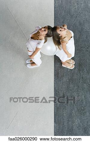 Teenage twin sisters standing back to back with heads touching, supporting fitness ball between them, high angle view View Large Photo Image Stock Image - Teenage twin sisters standing back to back with heads touching, supporting fitness ball between them, high angle view. Fotosearch