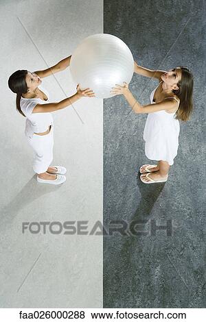 Teenage twin sisters standing face to face, holding up fitness ball together, viewed from directly above View Large Photo Image Stock Photo - Teenage twin sisters standing face to face, holding up fitness ball together, viewed from directly above. Fotosearch