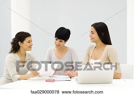 Three female professionals sitting at table, having discussion, one holding document View Large Photo Image Stock Photo - Three female professionals sitting at table, having discussion, one holding document. Fotosearch