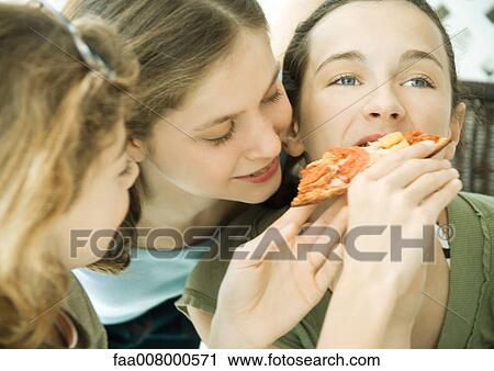 Stock Image - Three preteen girls, feeding friend pizza. Fotosearch