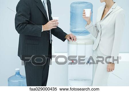 Two business colleagues standing by water cooler, cropped View Large Photo Image Stock Photography - Two business colleagues standing by water cooler, cropped. Fotosearch