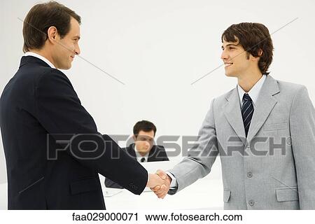 Two businessmen shaking hands, smiling at each other View Large Photo Image Stock Image - Two businessmen shaking hands, smiling at each other. Fotosearch