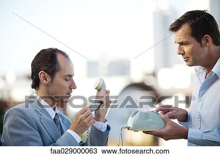Two businessmen standing face to face, looking at landline phone, side view View Large Photo Image Stock Image - Two businessmen standing face to face, looking at landline phone, side view. Fotosearch