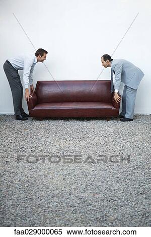 Two businessmen standing picking up sofa, looking at each other, side view View Large Photo Image Stock Photography - Two businessmen standing picking up sofa, looking at each other, side view. Fotosearch