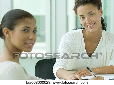 Two female coworkers, smiling at camera View Large Photo Image Stock Photo - Two female coworkers, smiling at camera. Fotosearch