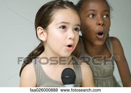 Two little girls singing into microphone together, close-up View Large Photo Image Stock Photo - Two little girls singing into microphone together, close-up. Fotosearch