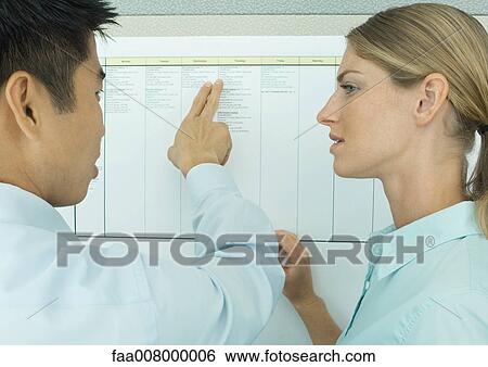 Two office workers looking at chart on wall View Large Photo Image Stock Photograph - Two office workers looking at chart on wall. Fotosearch
