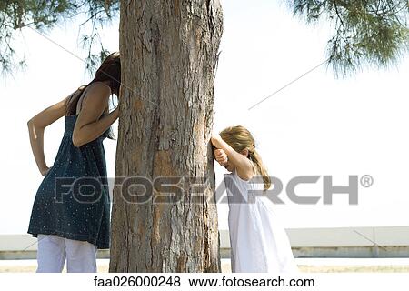 Two sisters playing hide-and-seek, one peeking around tree as the other counts View Large Photo Image Stock Photo - Two sisters playing hide-and-seek, one peeking around tree as the other counts. Fotosearch