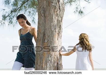 Two sisters walking around tree trunk, little girl touching tree with hand View Large Photo Image Stock Photograph - Two sisters walking around tree trunk, little girl touching tree with hand. Fotosearch