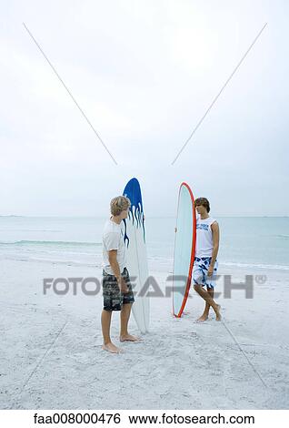 Two surfers standing on beach View Large Photo Image Stock Photograph - Two surfers standing on beach. Fotosearch