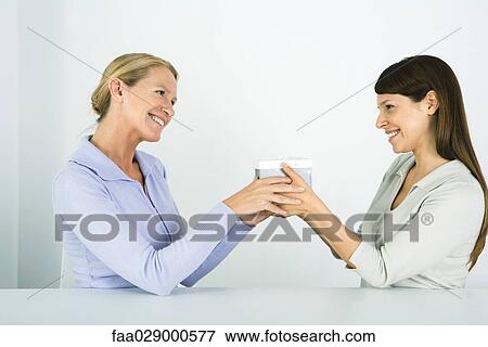 Two women face to face, exchanging gift, smiling at each other View Large Photo Image Stock Photo - Two women face to face, exchanging gift, smiling at each other. Fotosearch