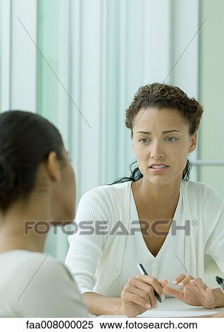 Two women having discussion at table, one holding pen View Large Photo Image Stock Photography - Two women having discussion at table, one holding pen. Fotosearch