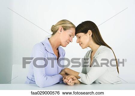 Stock Photograph - Two women holding hands, touching foreheads, eyes closed. Fotosearch