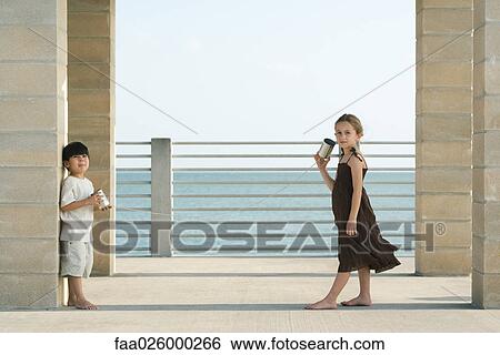 Stock Photograph - Two young friends playing with tin can phone together, girl looking at camera. Fotosearch