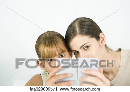 Stock Image - Woman and girl cheek to cheek, looking into hand mirrors. Fotosearch