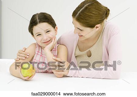 Woman and girl, girl holding apple, smiling at camera View Large Photo Image Picture - Woman and girl, girl holding apple, smiling at camera. Fotosearch