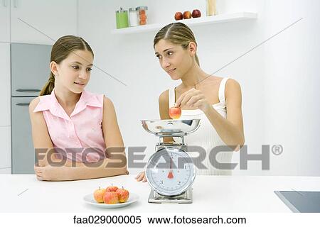 Woman and girl in kitchen, weighing apple View Large Photo Image Stock Photography - Woman and girl in kitchen, weighing apple. Fotosearch