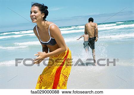 Stock Photo - Woman at the beach, smiling, man and child splashing in the background. Fotosearch