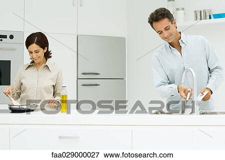 Stock Photo - Woman cooking while man washes dishes. Fotosearch