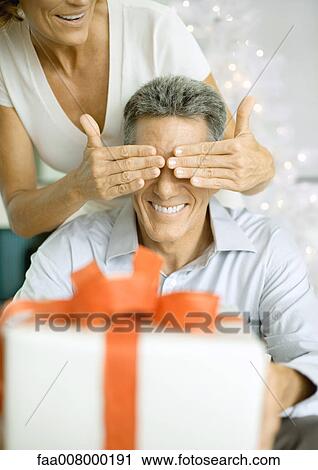 Woman covering man's eyes before giving him christmas gift View Large Photo Image Stock Image - Woman covering man's eyes before giving him christmas gift. Fotosearch