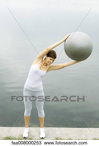 Stock Image - Woman exercising with fitness ball, next to lake. Fotosearch