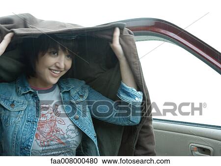 Woman getting out of car, holding up jacket over head View Large Photo Image Stock Image - Woman getting out of car, holding up jacket over head. Fotosearch