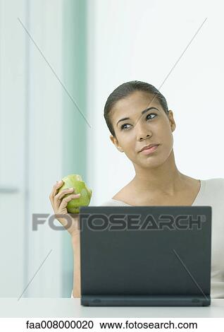 Woman holding apple, sitting at laptop View Large Photo Image Stock Image - Woman holding apple, sitting at laptop. Fotosearch