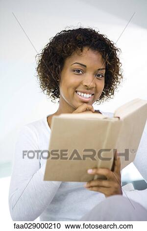 Woman holding book in one hand, other hand under chin, smiling at camera View Large Photo Image Stock Image - Woman holding book in one hand, other hand under chin, smiling at camera. Fotosearch