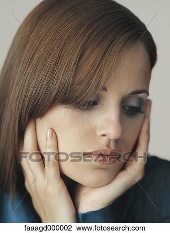 Stock Image - Woman holding face in hands, looking down, portrait. Fotosearch